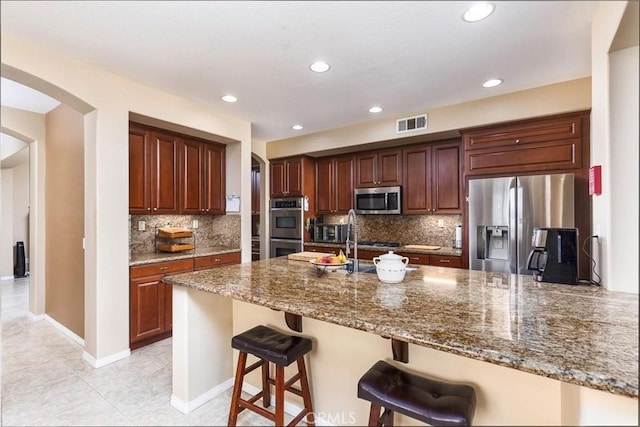 kitchen featuring visible vents, a peninsula, dark stone counters, arched walkways, and stainless steel appliances