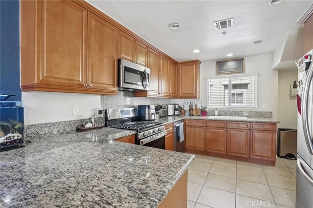2810 Green River Rd Unit 103, Corona, CA 92882 - kitchen with stainless steel appliances, a sink, brown cabinets, light stone counters, and light tile patterned floors