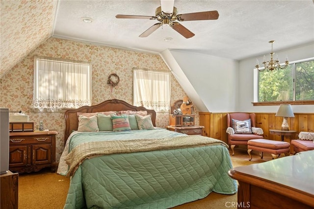 carpeted bedroom with a textured ceiling, wainscoting, wallpapered walls, ceiling fan, and vaulted ceiling