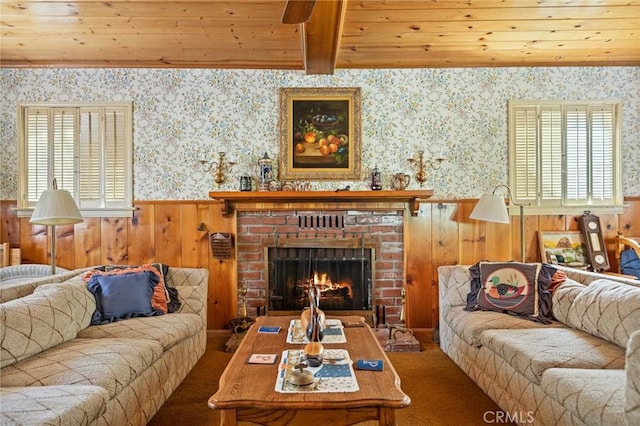 carpeted living room with a wainscoted wall, a brick fireplace, wooden ceiling, and wallpapered walls