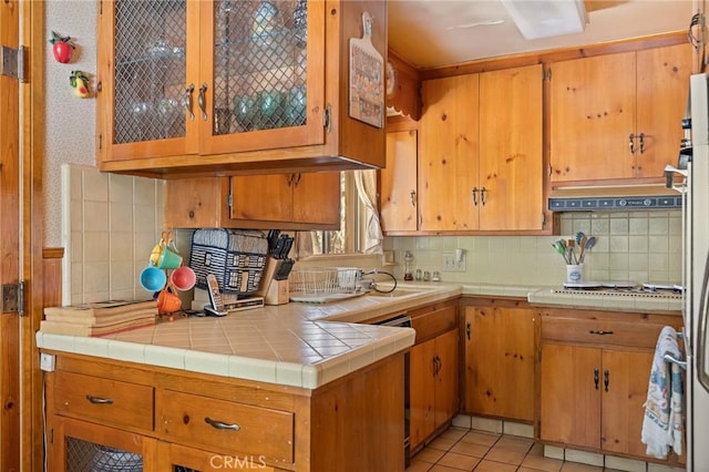 kitchen featuring light tile patterned floors, backsplash, brown cabinetry, and white cooktop