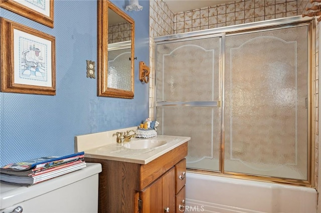 bathroom featuring toilet, wallpapered walls, vanity, and shower / bath combination with glass door