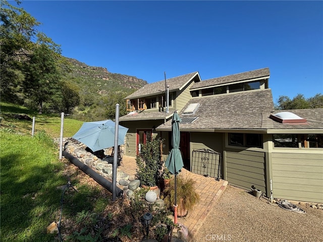 view of home's exterior with a mountain view, a shingled roof, and a patio area