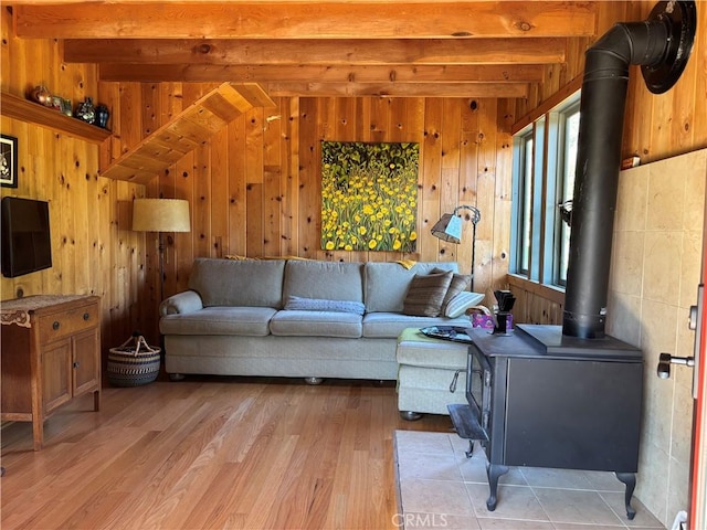living area with beamed ceiling, wood walls, light wood finished floors, and a wood stove