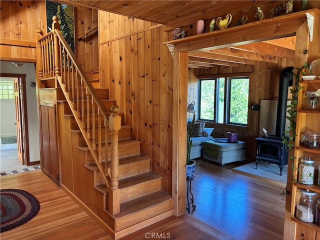 stairway featuring wood-type flooring, wooden walls, and a wood stove