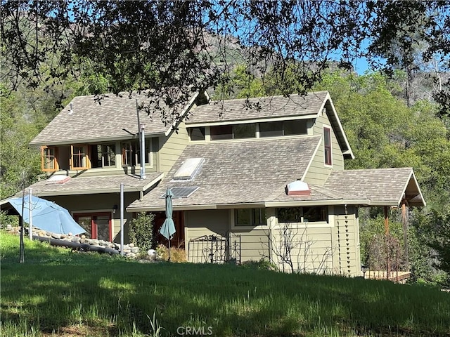 back of house with roof with shingles and a yard
