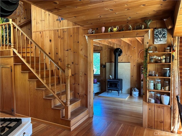 stairs with wood-type flooring, wood walls, a wood stove, and wooden ceiling