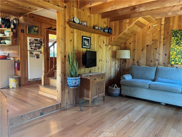 living area featuring light wood-style floors, stairway, wood walls, and beam ceiling