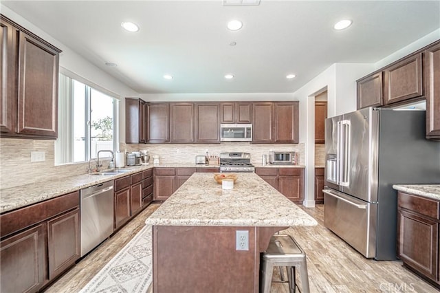 148 Mesquite Ct, Calimesa, CA 92320 - kitchen featuring stainless steel appliances, a kitchen island, a kitchen breakfast bar, light wood-style flooring, and light stone counters