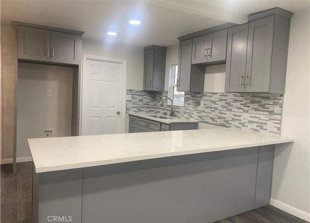 kitchen featuring a peninsula, gray cabinets, dark wood-style flooring, a sink, and decorative backsplash