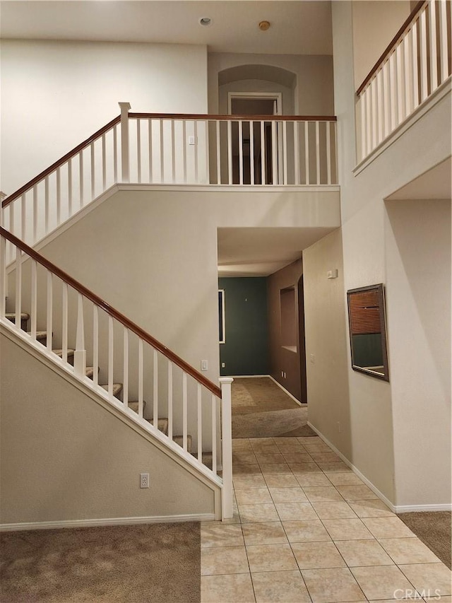 stairway with carpet floors, tile patterned floors, a towering ceiling, and baseboards