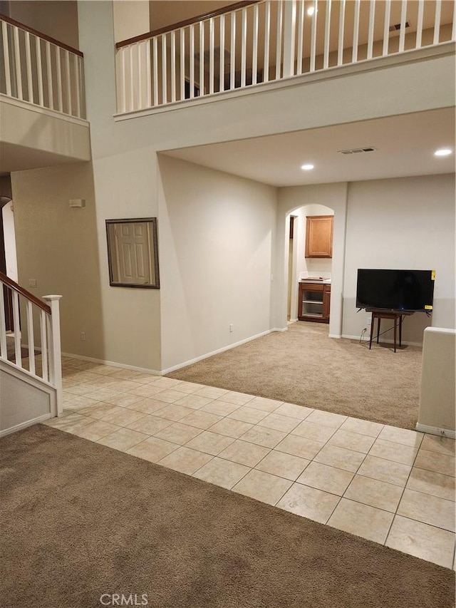 unfurnished living room featuring light carpet, light tile patterned floors, a towering ceiling, and visible vents