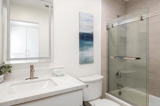 full bath featuring combined bath / shower with glass door, toilet, vanity, and visible vents