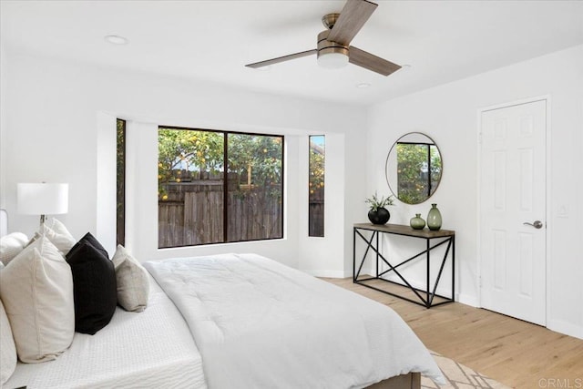 bedroom with light wood-type flooring, multiple windows, baseboards, and a ceiling fan