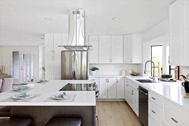 kitchen with light countertops, dishwashing machine, freestanding refrigerator, island range hood, and a sink