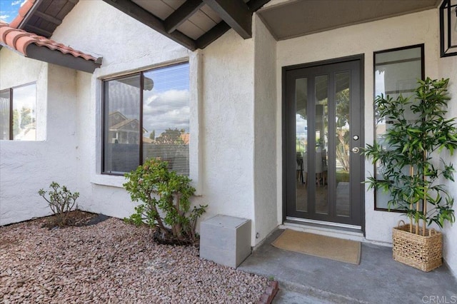 entrance to property featuring a tiled roof, french doors, and stucco siding