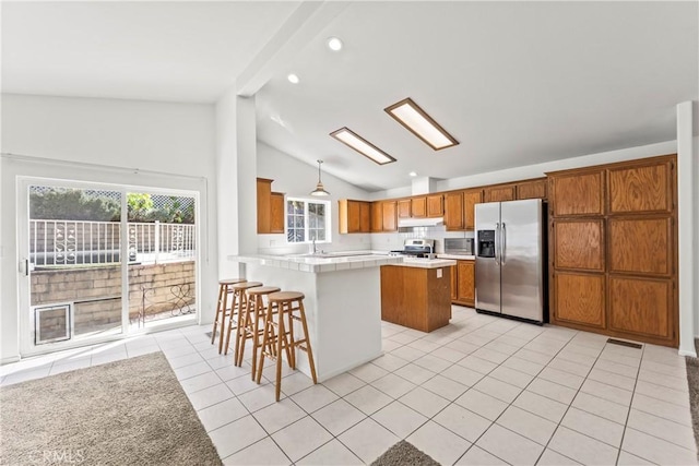 kitchen featuring lofted ceiling, a peninsula, light tile patterned flooring, appliances with stainless steel finishes, and brown cabinets