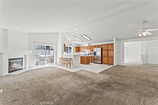 unfurnished living room featuring a ceiling fan, lofted ceiling with beams, light tile patterned flooring, a fireplace, and light carpet