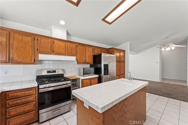 kitchen featuring under cabinet range hood, tile countertops, decorative backsplash, stainless steel appliances, and a sink