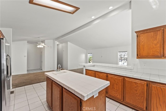 kitchen with open floor plan, lofted ceiling, light tile patterned floors, stainless steel fridge, and a sink