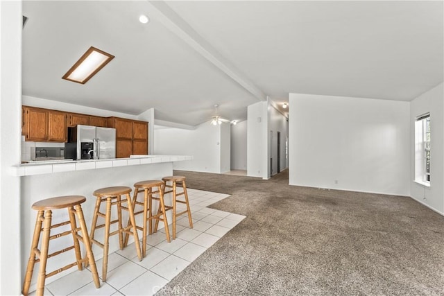 kitchen featuring tile countertops, vaulted ceiling with beams, stainless steel fridge with ice dispenser, a kitchen breakfast bar, and open floor plan