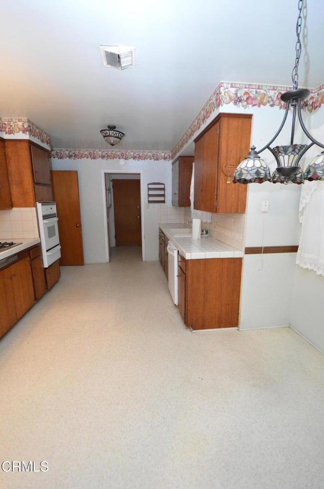 kitchen featuring visible vents, tile counters, decorative backsplash, brown cabinetry, and white appliances