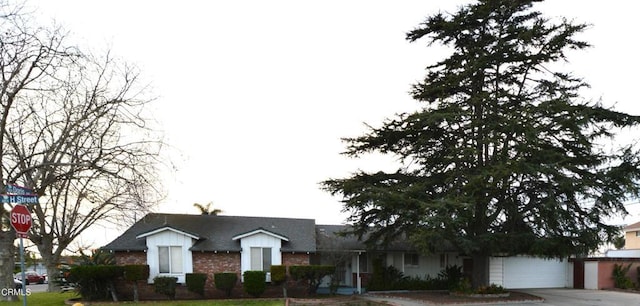view of front of house with brick siding, driveway, an attached garage, and roof with shingles