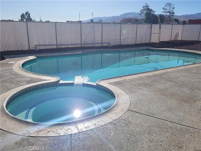 view of pool featuring a mountain view, fence, and a pool with connected hot tub