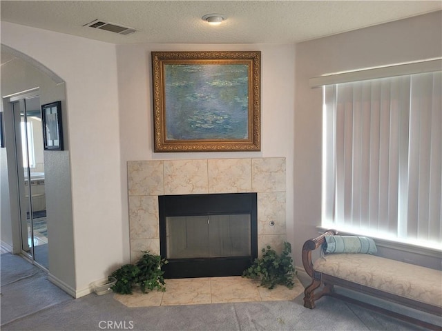 carpeted living area featuring visible vents, arched walkways, a textured ceiling, and a tile fireplace