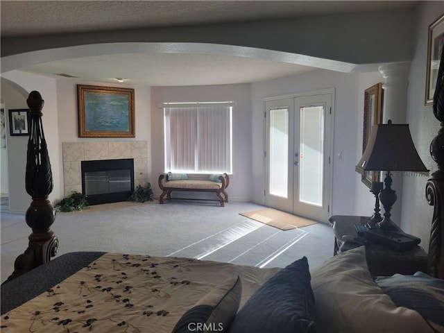 carpeted living room featuring visible vents, arched walkways, french doors, a textured ceiling, and a tiled fireplace