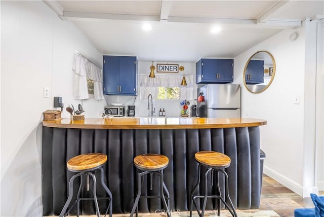 interior space with blue cabinetry, freestanding refrigerator, a sink, a kitchen breakfast bar, and light wood-type flooring