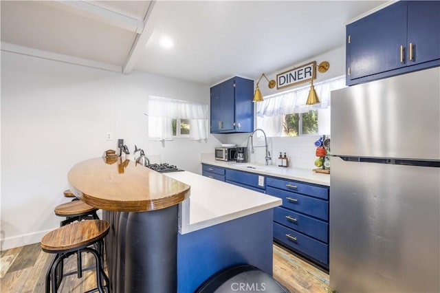 kitchen with tasteful backsplash, blue cabinetry, light countertops, light wood-style flooring, and freestanding refrigerator