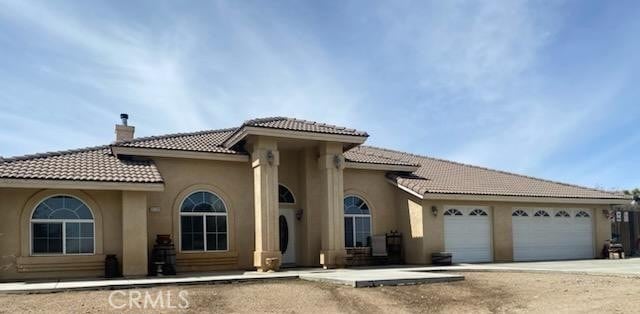 mediterranean / spanish-style house with a tile roof, stucco siding, a garage, a chimney, and driveway