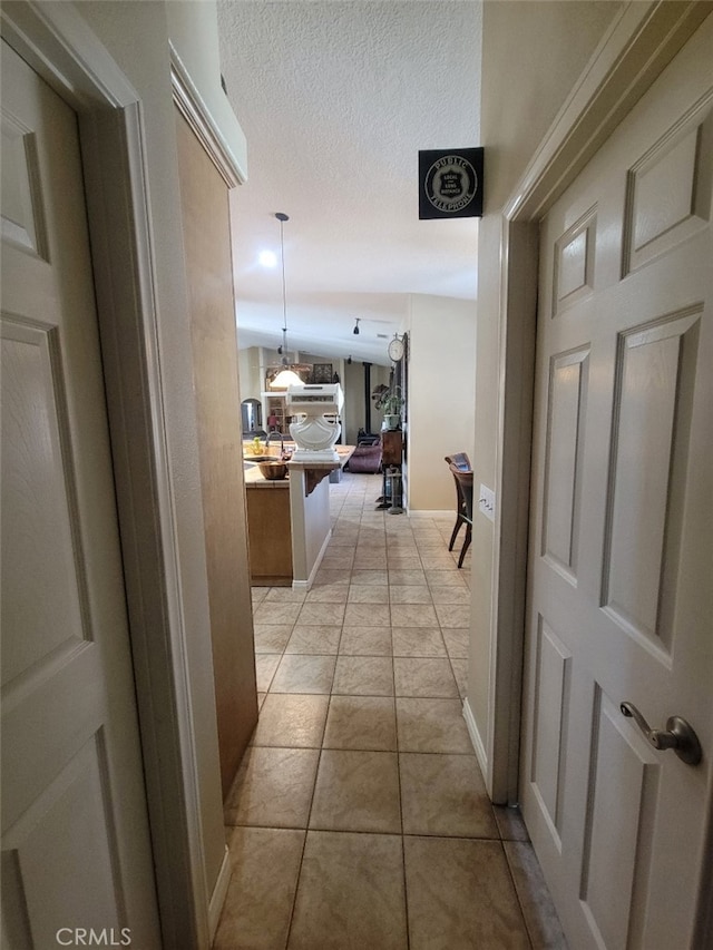hallway with light tile patterned flooring, a textured ceiling, and baseboards