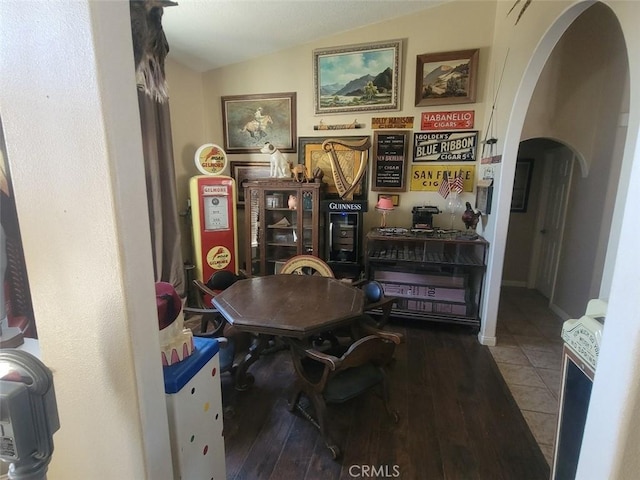 dining area featuring arched walkways, vaulted ceiling, and hardwood / wood-style floors