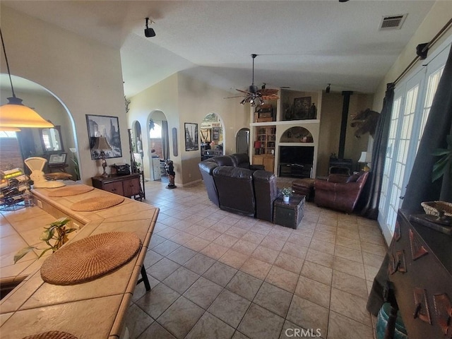 tiled living room featuring arched walkways, lofted ceiling, a ceiling fan, and a wood stove