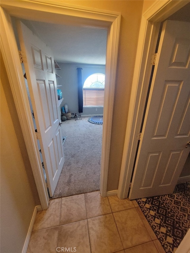 corridor featuring light carpet, light tile patterned floors, and baseboards