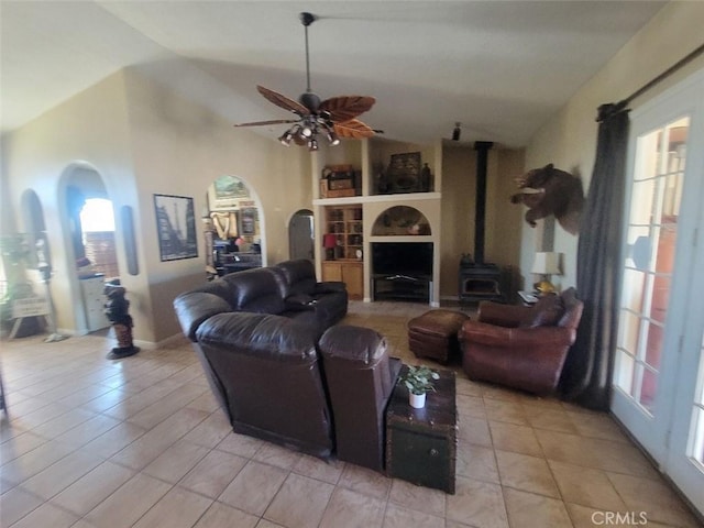 living area with lofted ceiling, a wood stove, a ceiling fan, built in features, and light tile patterned floors