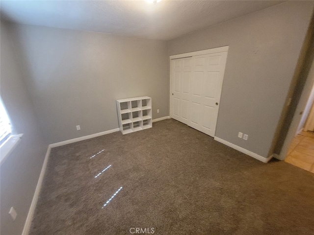 unfurnished bedroom featuring dark colored carpet, a closet, and baseboards