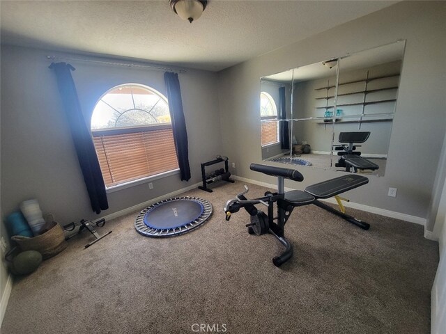 exercise room featuring a textured ceiling, carpet floors, and baseboards