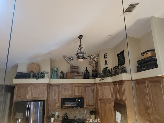 kitchen view of freestanding refrigerator, brown cabinets, pendant lighting, light countertops, and a chandelier