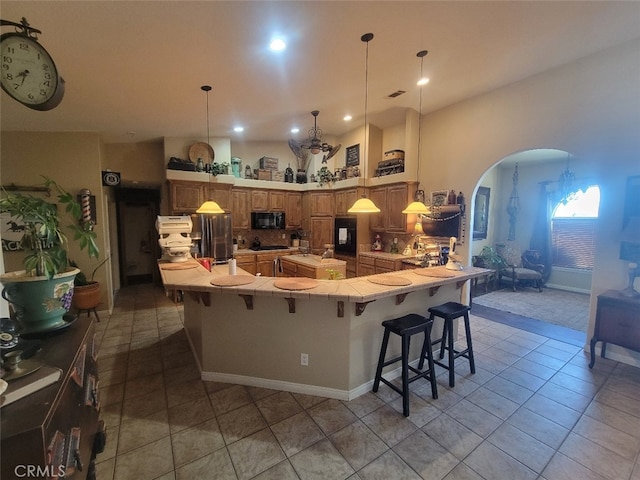 kitchen with black microwave, arched walkways, a kitchen bar, a peninsula, and light tile patterned floors