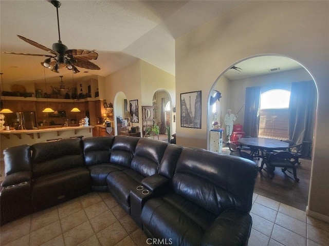 living area with tile patterned flooring, arched walkways, ceiling fan, and vaulted ceiling