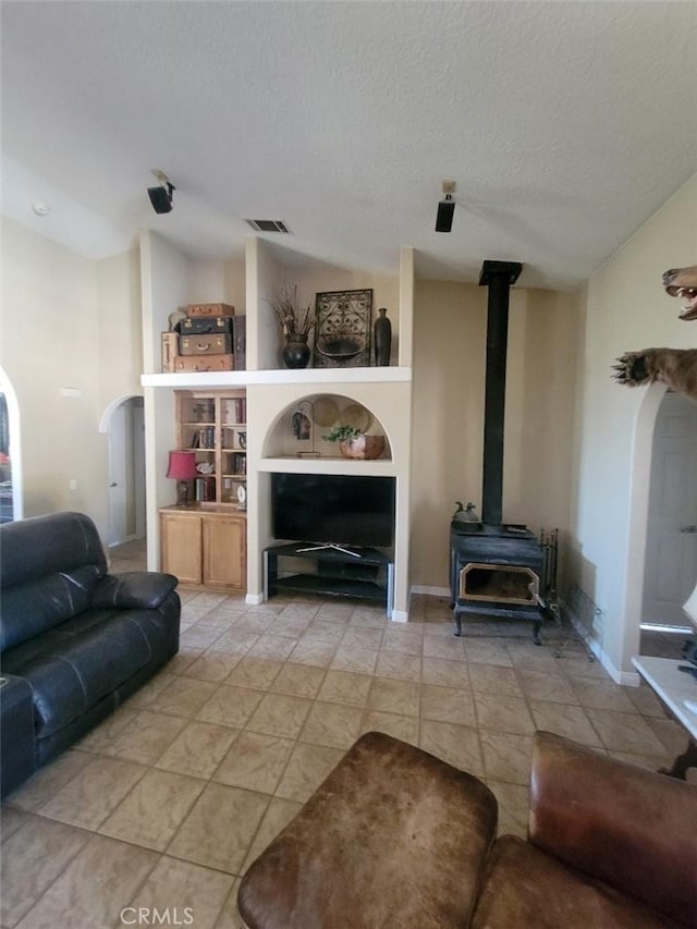 living room with arched walkways, a wood stove, a textured ceiling, and baseboards