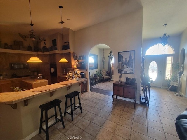 kitchen with tile countertops, light tile patterned floors, arched walkways, a kitchen breakfast bar, and a towering ceiling