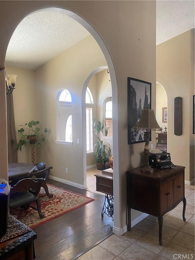 foyer with a textured ceiling, arched walkways, and baseboards