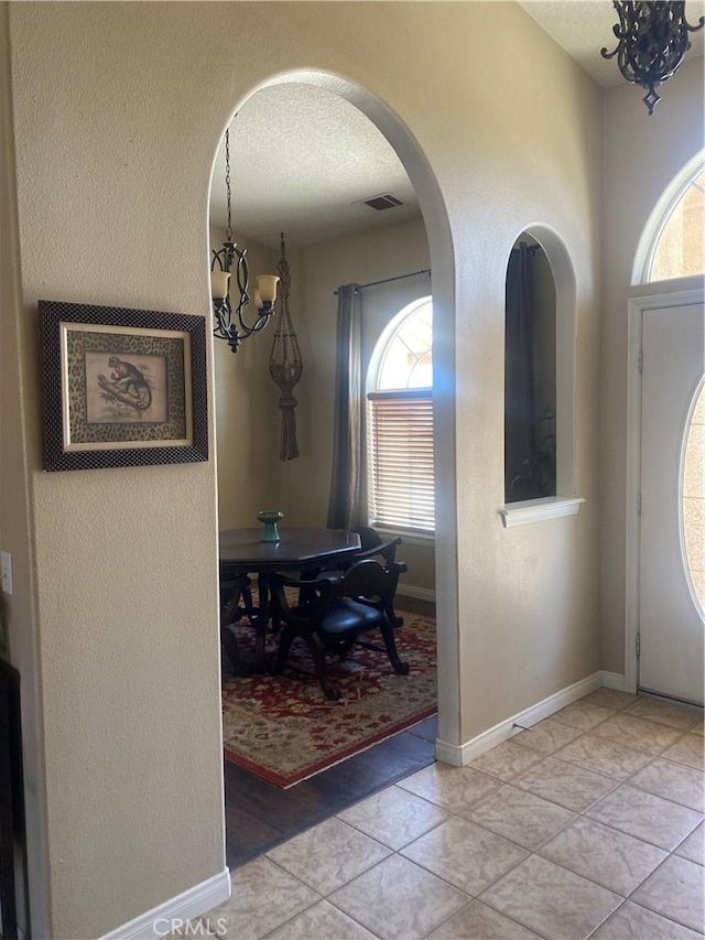 foyer entrance featuring a chandelier, plenty of natural light, arched walkways, a textured ceiling, and baseboards
