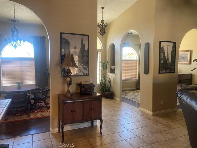hall with tile patterned flooring, a chandelier, baseboards, a textured ceiling, and high vaulted ceiling