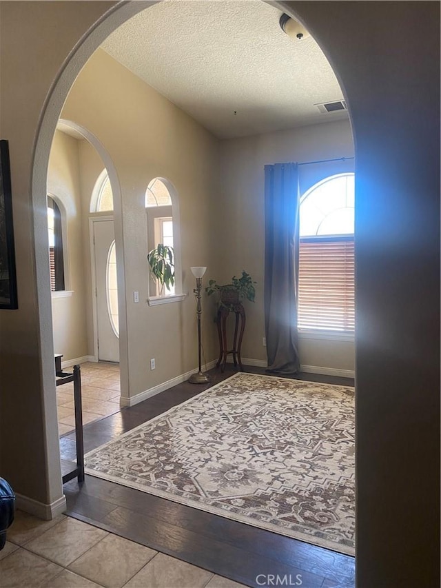 entrance foyer featuring healthy amount of natural light, a textured ceiling, arched walkways, wood finished floors, and baseboards