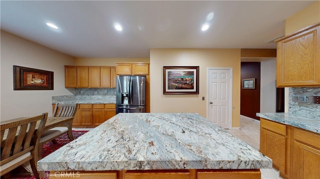 kitchen featuring light stone counters, a kitchen island, tasteful backsplash, recessed lighting, and stainless steel fridge
